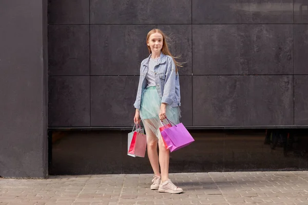 Молодая девушка в джинсах и юбке с покупками в руках в полном росте. — стоковое фото