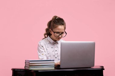 Gözlüklü ve at kuyruklu bir kız tahta bir masada oturuyor.