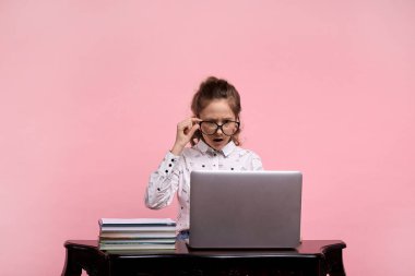 Şaşırmış güzel bir genç kız bir dizüstü bilgisayarla masada oturuyor.