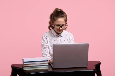 Gözlüklü ve at kuyruklu bir kız tahta bir masada oturuyor.