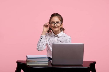 Gözlüklü ve kuyruğunda kıl olan kız tahta bir masada oturuyor.
