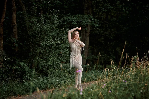 Kvinna i en beige klänning dansar på ett fält med blommor, makram i kläder. — Stockfoto