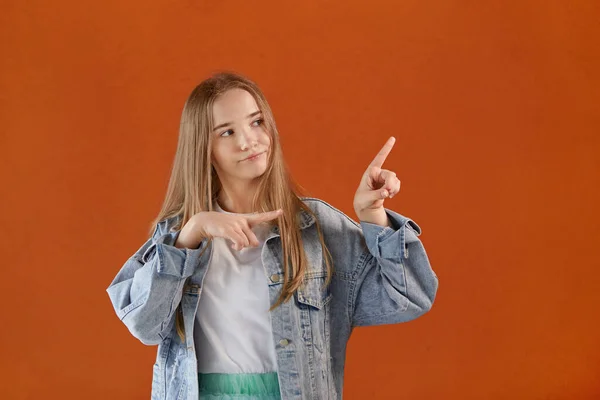 Een mooi jong meisje wijst haar hand naar de oranje achtergrond. — Stockfoto