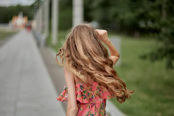Långt vackert vågigt blont hår. Sommaren i parken. Vacker rosa klänning. — Stockfoto