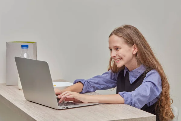 Una chica con el pelo largo y rubio ondulado está estudiando en línea con un ordenador portátil. — Foto de Stock
