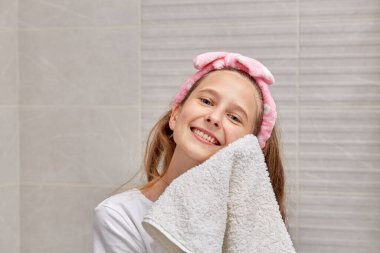 Sarışın bir kız beyaz bir Terry havlusuyla yüzünü siliyor. Sabah rutini.