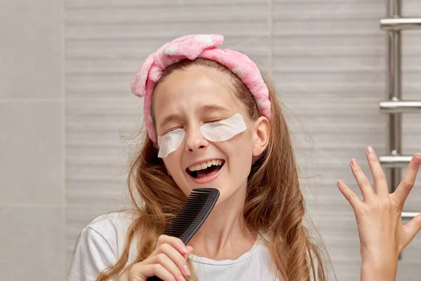 Uma menina com manchas de olhos médicos segura um pente na mão e canta. — Fotografia de Stock