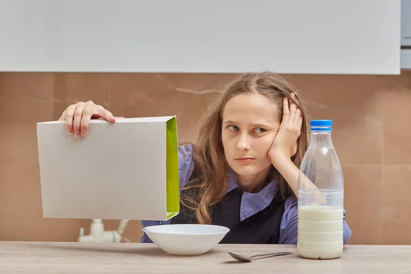 Una triste ragazza bionda versa cornflakes da un pacchetto di cereali. — Foto Stock