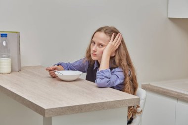 Yorgun ve üzgün bir kız sabahları mısır gevreğini sütle yer ve kameraya bakar..