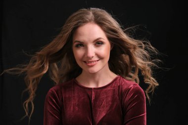 Uzun dalgalı saçlı, mutlu, genç esmer kadın gülümseyip kameraya bakıyor..