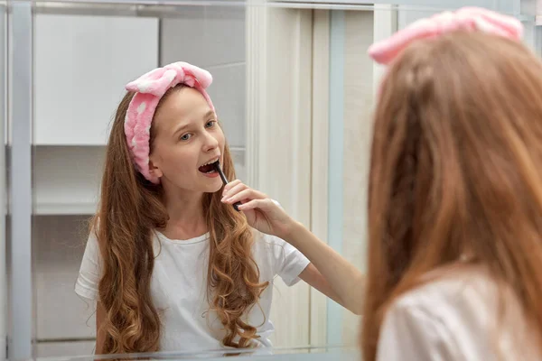 Menina no banheiro escovando os dentes de manhã em uma bandagem na cabeça. — Fotografia de Stock