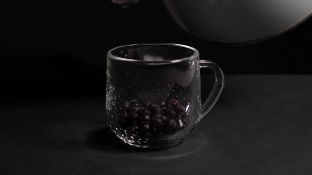 Heißes Wasser wird in eine transparente Tasse mit schwarzen Johannisbeeren gegossen. — Stockvideo