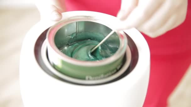 Den kvinnliga handen av en professionell kosmetolog rör varmt vax av grön färg. — Stockvideo