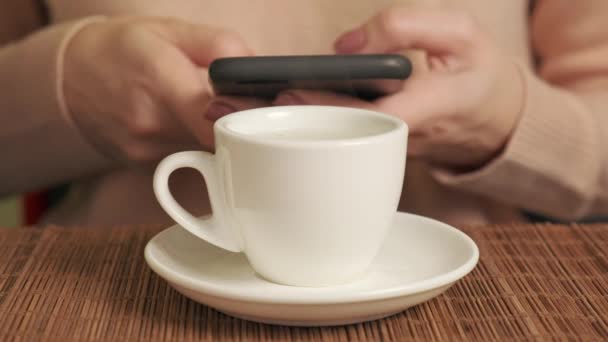 Mains féminines avec téléphone portable dans les mains et boire du café en tasse blanche. — Video