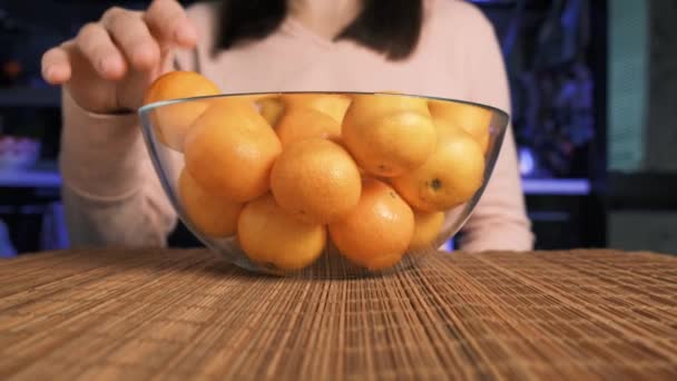 Una mujer pone en un plato de vidrio en una estera de bambú, mandarinas de naranja jugosas maduras. — Vídeos de Stock