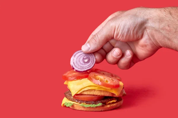 Ik kook een grote Burger. Hand ringen van ui op de tomaten. Rode achtergrond. — Stockfoto