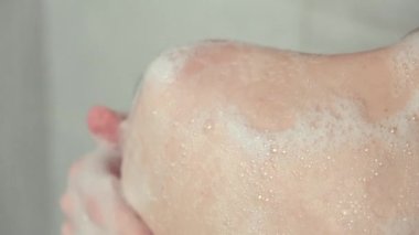 Banyoda vücudunu köpükle yıkayan genç bir kadının yakın çekimi..