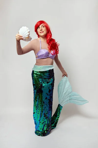 A woman in a mermaid costume holds a shell in one hand and a tail in the other. — Stock Photo, Image