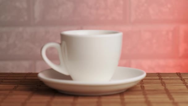 Taza de cerámica blanca en la estera de bambú de mesa. Fondo rosa y pared de ladrillo. — Vídeos de Stock