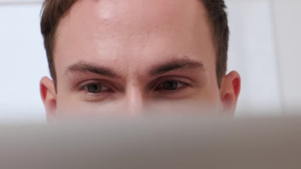 Belos olhos de um jovem trabalhando em casa online com um laptop. — Vídeo de Stock