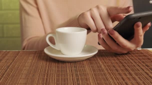 Una mano di donne beve caffè e comunica online utilizzando un telefono cellulare. — Video Stock