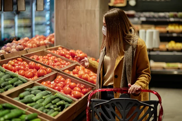 Μια νεαρή γυναίκα στο σούπερ μάρκετ διαλέγει ντομάτες με καρότσι για ψώνια.. — Φωτογραφία Αρχείου