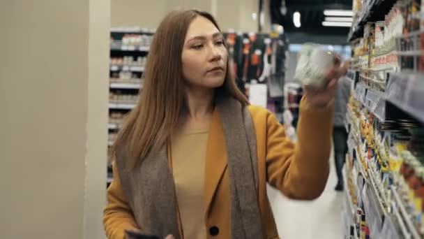 Femme fait du shopping dans un supermarché et numérise des codes à barres avec smartphone. — Video