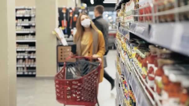 A woman in a supermarket wearing a medical mask scans the barcode on the product — Stock Video