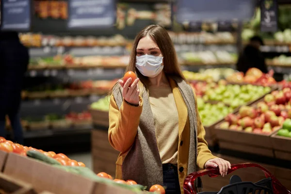 Μια γυναίκα με ιατρική μάσκα σε σούπερ μάρκετ διαλέγει λαχανικά.. — Φωτογραφία Αρχείου
