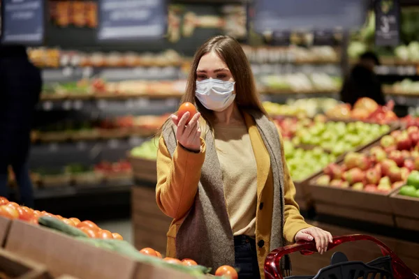 Süpermarkette tıbbi maskeli bir kadın sebze seçer..