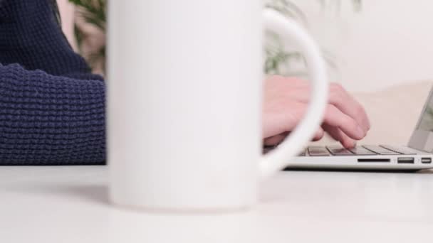 En la mesa hay una taza de café y un hombre trabajando en la oficina en una computadora portátil. — Vídeos de Stock