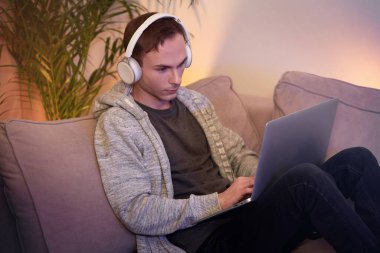 Bir adam kulaklıkla kanepede uzanıyor müzik dinliyor, çalışıyor, internetten..