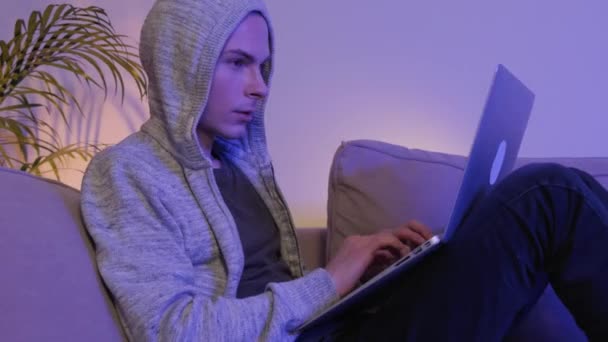 Un hombre con interés juega en un portátil por la noche acostado en casa en el sofá. — Vídeos de Stock