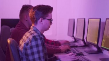 Gömlekli programcılar ofiste oturup bilgisayar başında iş konuşuyorlar..