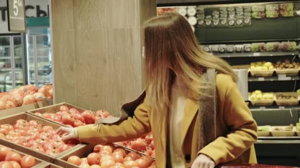 Žena v kabátě sbírá čerstvá rajčata v obchodě v lékařské masce. — Stock video