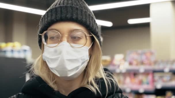 Een blonde vrouw heeft haar bril verward in een supermarkt met een medisch masker.. — Stockvideo