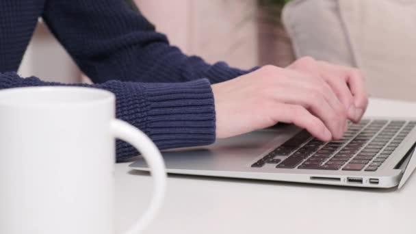 En man händer skriver text på en bärbar dator och det finns en kopp kaffe bredvid. — Stockvideo