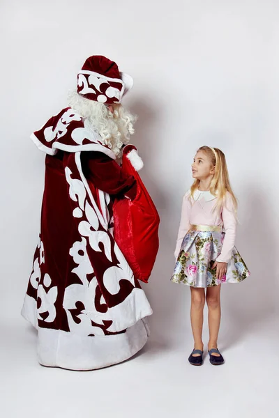 Papai Noel em pleno crescimento com um saco de presentes tira um presente para uma menina. — Fotografia de Stock