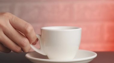 Bir kadının eli masaya beyaz bir fincan kahve koyar. Sağdaki kırmızı ışık..