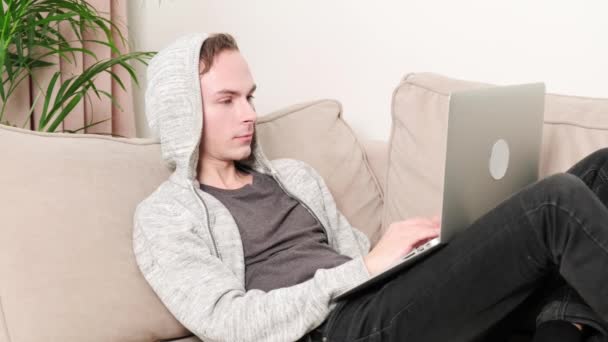 L'homme travaille couché sur le canapé avec l'ordinateur portable et ferme les yeux pour se reposer. — Video