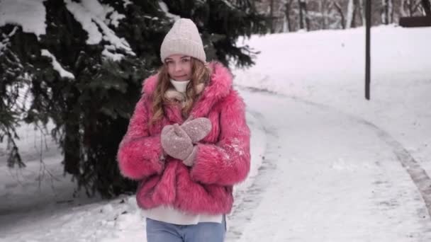 Egy gyönyörű nő rózsaszín bundában sétál át a téli parkon. Téli játékok. — Stock videók