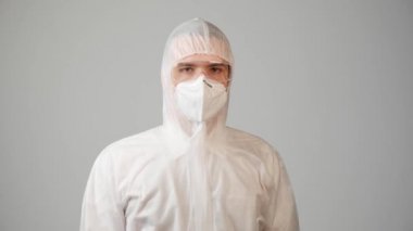 Tıbbi kıyafetli bir doktor kameraya bakar ve el hareketi yapar..