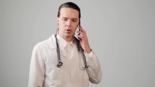 ドレッシングのガウンと白いシャツの男の医者が携帯電話で話してる. — ストック動画