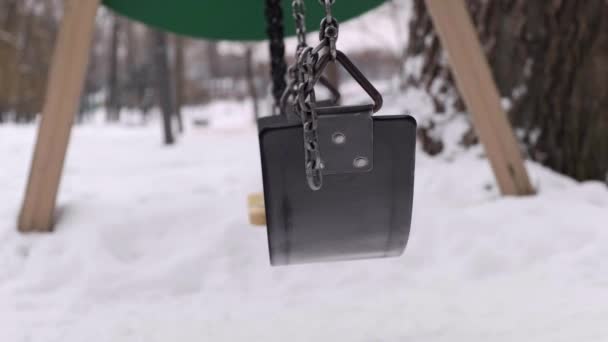 Primer plano de un columpio balanceándose solo en un parque de invierno cubierto de nieve. — Vídeo de stock