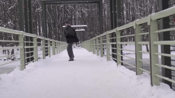 Une jeune femme traverse joyeusement un pont au-dessus d'une rivière. Un hiver froid et enneigé. — Video