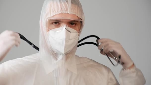 Een mannelijke arts in een beschermend medisch pak gebruikt een fonendoscoop. — Stockvideo