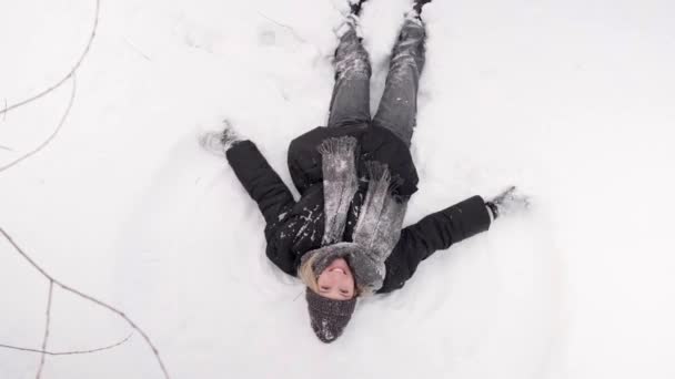 Вид зверху на щасливу красиву жінку робить сніговий ангел взимку. 4k відео . — стокове відео
