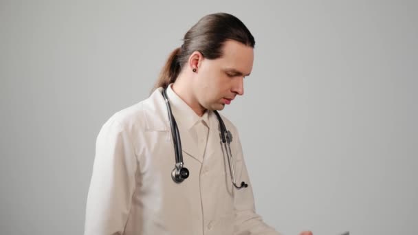 Ein junger Arzt im Laborkittel und weißem Hemd nimmt einen dringenden Anruf entgegen. — Stockvideo