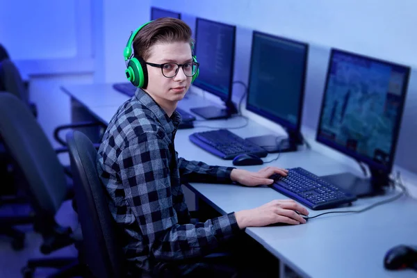 Seorang gamer pria dengan headphone hijau terang dan kacamata, melihat ke kamera. Stok Lukisan  