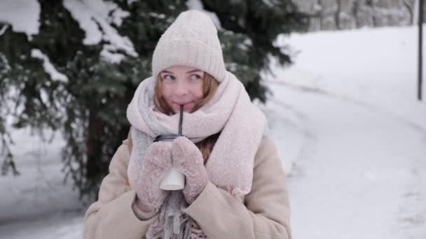 Krásná mladá blondýna žena pití horký koktejl zima procházky v parku. — Stock video